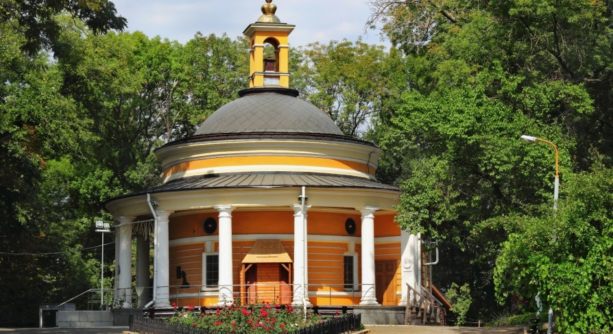 Askoldova Mohyla in Kyiv - iconic St. Nicholas Rotunda Church featuring bright yellow walls and white columns nestled among the peaceful park trees