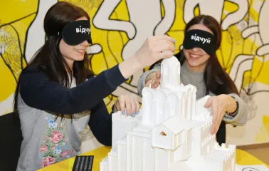 Muzei u Temriavi in Kyiv - smiling visitors wearing black eye masks exploring a 3D white architectural model of a church by touch