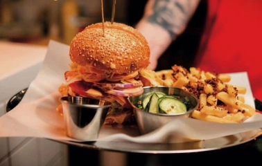 True Burger Bar - close-up of a plated gourmet burger served with fries and pickles