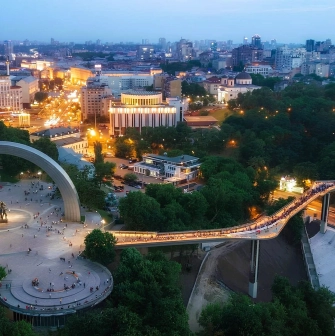 Aerial night view of the illuminated Glass Bridge and Arch of Freedom in Kyiv
