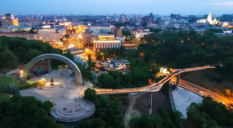 Aerial night view of the illuminated Glass Bridge and Arch of Freedom in Kyiv