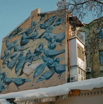 Wide view of the Herald of Life crow mural on a brick building in Kyiv