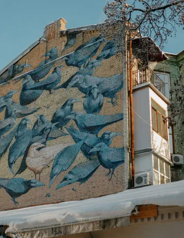 Wide view of the Herald of Life crow mural on a brick building in Kyiv