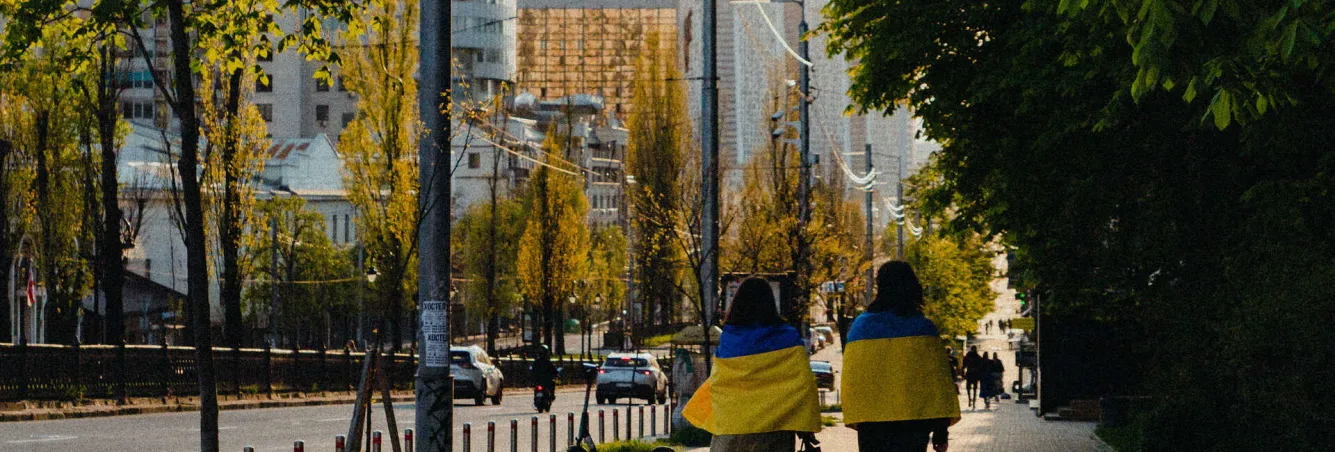 Two women wrapped in Ukrainian flags walking down Lesya Ukrainka Boulevard in Kyiv