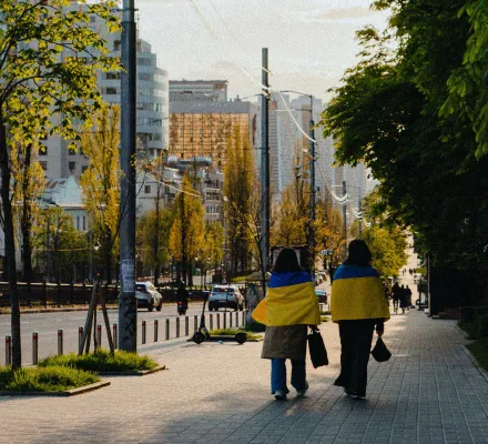 Two women wrapped in Ukrainian flags walking down Lesya Ukrainka Boulevard in Kyiv