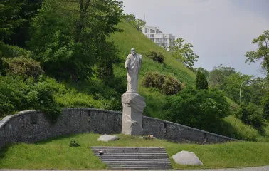 Askoldova Mohyla in Kyiv - majestic stone statue of Apostle Andrew standing on a rock pedestal against the steep lush green slope of the hill