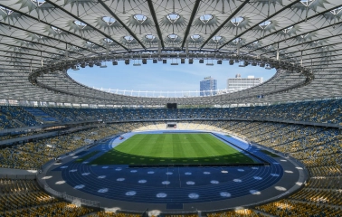 NSC Olimpiyskiy in Kyiv - majestic interior view of the stadium featuring the iconic glass roof structure with a central opening above the green pitch and thousands of seats