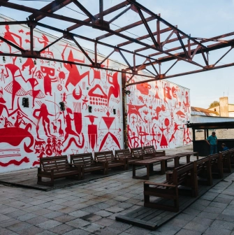 Lavra Gallery in Kyiv - outdoor terrace with wooden benches and a wall covered in red primitive murals