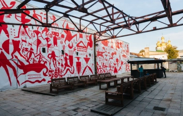 Lavra Gallery in Kyiv - outdoor terrace with wooden benches and a wall covered in red primitive murals