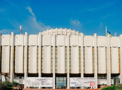 Ukrainskyi Dim in Kyiv - massive white modernist building with vertical lines and flags against the blue sky
