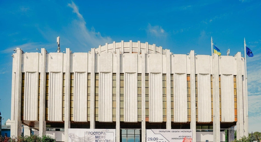 Ukrainskyi Dim in Kyiv - massive white modernist building with vertical lines and flags against the blue sky