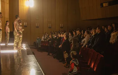 Teatr Voiennykh Dii in Kyiv - theatrical performance with shirtless actors in camouflage pants standing on a stage before the audience