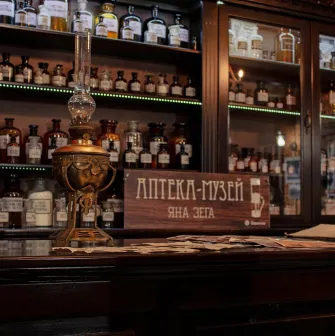 Pharmacy Museum in Kyiv - close-up of a wooden counter featuring a vintage kerosene lamp and a sign reading "Jan Zeh Pharmacy Museum" amidst glass bottles