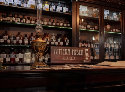 Pharmacy Museum in Kyiv - close-up of a wooden counter featuring a vintage kerosene lamp and a sign reading "Jan Zeh Pharmacy Museum" amidst glass bottles