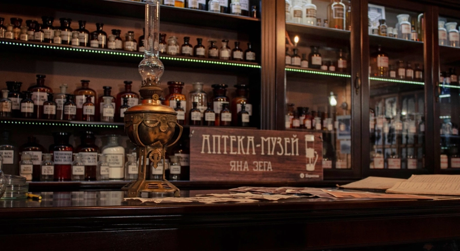 Pharmacy Museum in Kyiv - close-up of a wooden counter featuring a vintage kerosene lamp and a sign reading "Jan Zeh Pharmacy Museum" amidst glass bottles