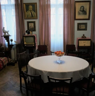 Muzei Tychyny in Kyiv - dining room area featuring a round table with apples, vintage furniture, a retro television set, and portraits on the light blue walls