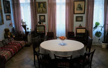 Muzei Tychyny in Kyiv - dining room area featuring a round table with apples, vintage furniture, a retro television set, and portraits on the light blue walls