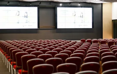 Великий конференц-зал із рядами крісел та екранами для презентацій