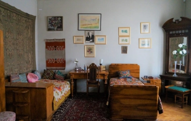 Muzei Tychyny in Kyiv - cozy historic bedroom featuring two wooden single beds with colorful covers, a writing desk, and walls adorned with framed artwork