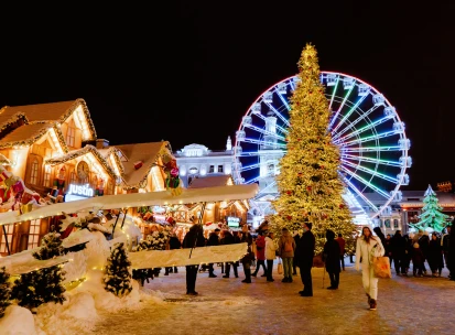 Christmas fair on Kontraktova Square in Kyiv - festive market with a large illuminated Christmas tree, Ferris wheel, and visitors walking among decorated wooden stalls at night