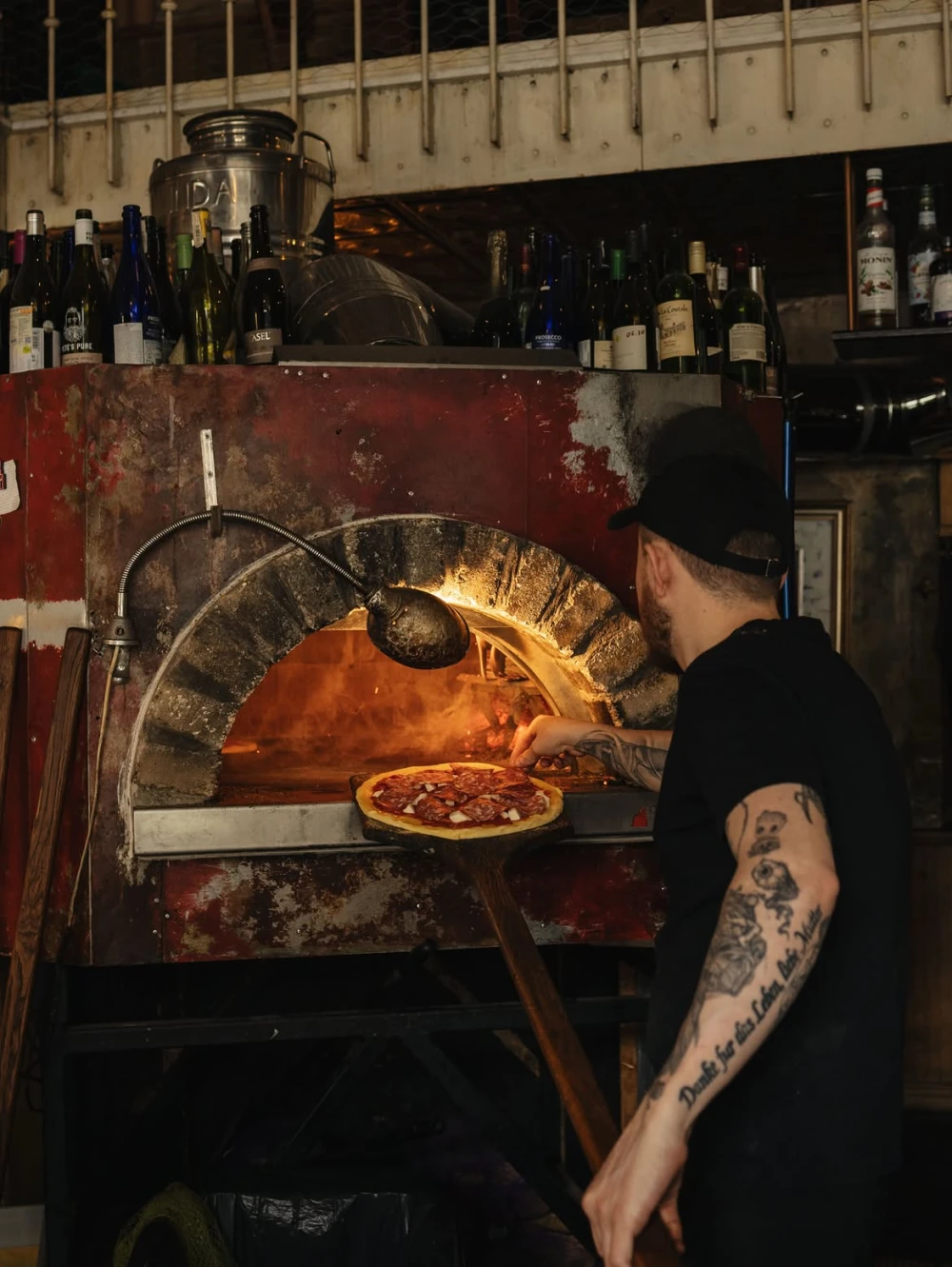 Pizzaiolo baking pizza in the wood-fired oven at Mimosa Brooklyn Pizza