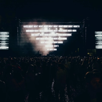 Art-zavod Platforma in Kyiv - dark silhouette of the crowd facing the stage illuminated by blinding white digital text at night