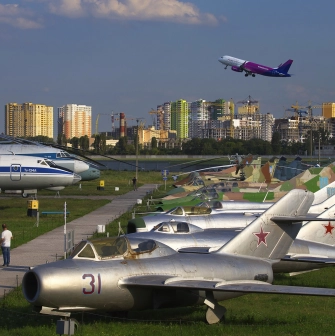 Aviation Museum in Kyiv - row of vintage silver military jets parked on the grass with a modern Wizz Air passenger plane taking off in the blue sky