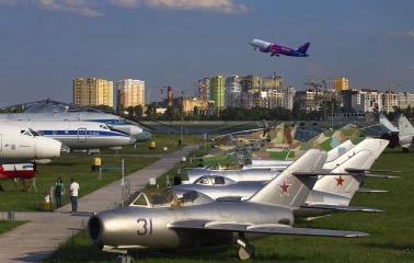 Aviation Museum in Kyiv - row of vintage silver military jets parked on the grass with a modern Wizz Air passenger plane taking off in the blue sky