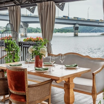 Khutorets na Dnipri – elegant wooden table with green napkins on the river terrace overlooking the Dnipro and bridge