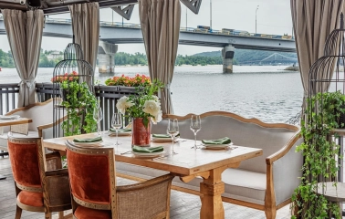 Khutorets na Dnipri – elegant wooden table with green napkins on the river terrace overlooking the Dnipro and bridge