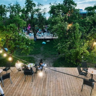 Vyava in Kyiv - outdoor wooden terrace with tables and chairs illuminated by string lights overlooking a green garden area