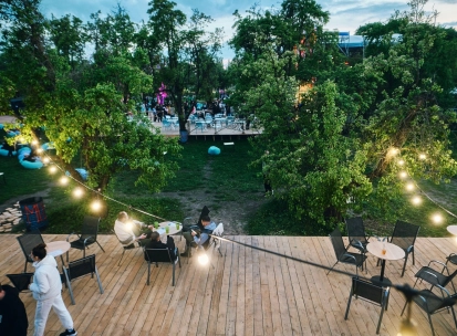 Vyava in Kyiv - outdoor wooden terrace with tables and chairs illuminated by string lights overlooking a green garden area