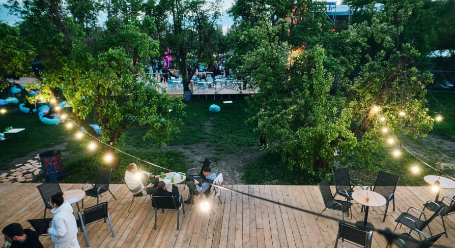 Vyava in Kyiv - outdoor wooden terrace with tables and chairs illuminated by string lights overlooking a green garden area